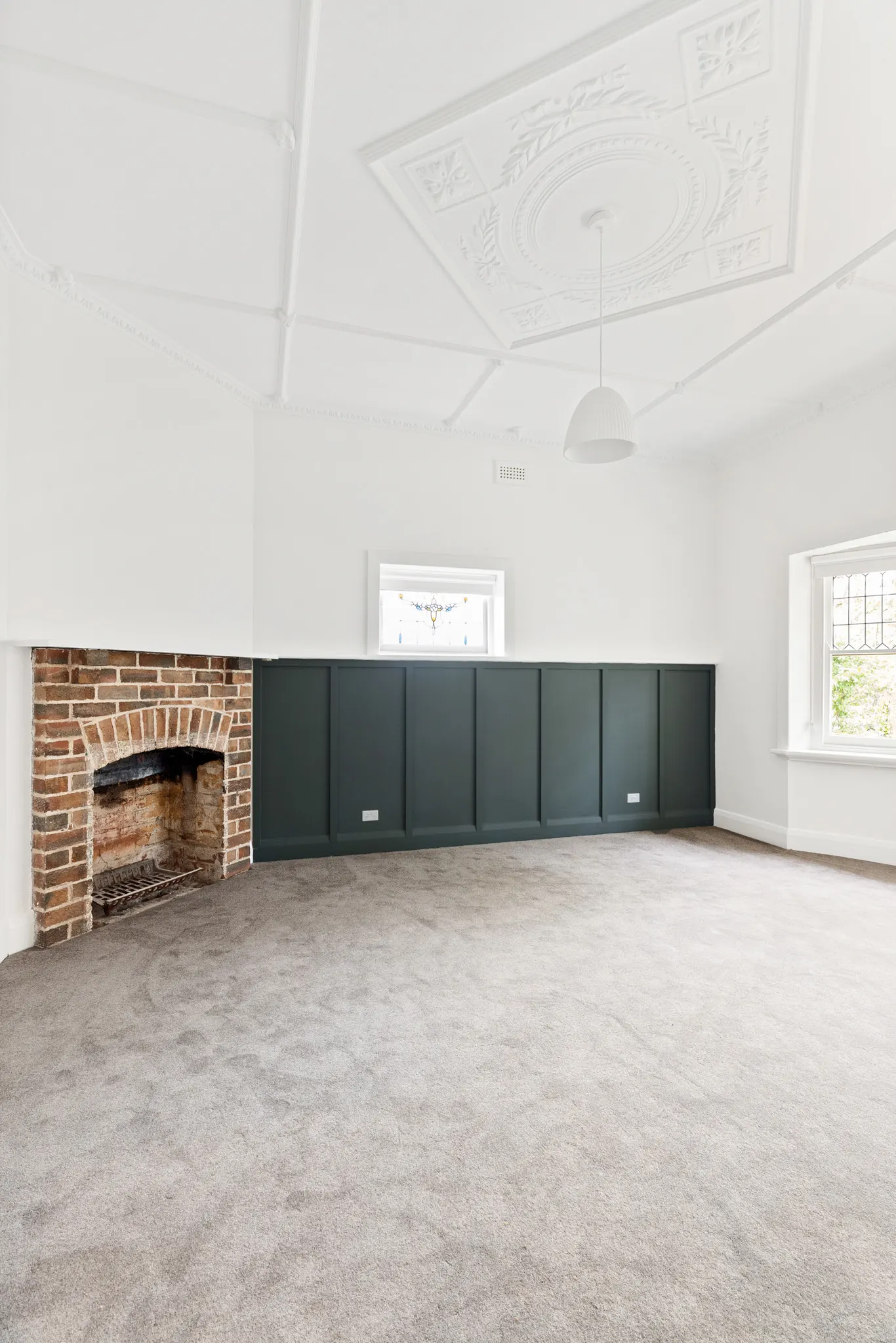 Original brick fireplace and dark green panelling beneath an ornate plaster ceiling