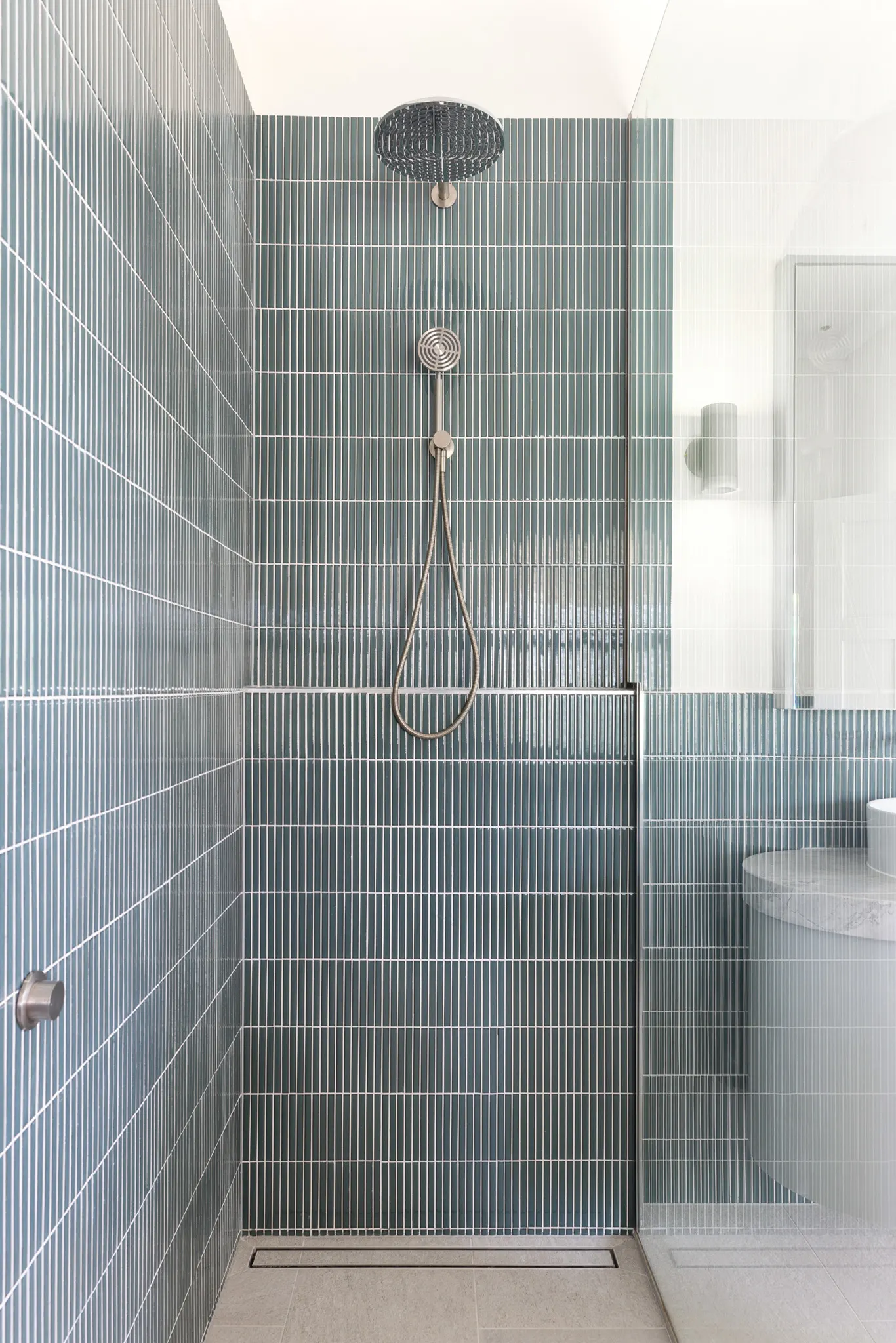 Shower recess lined in green finger tiles with a rain head and hand shower