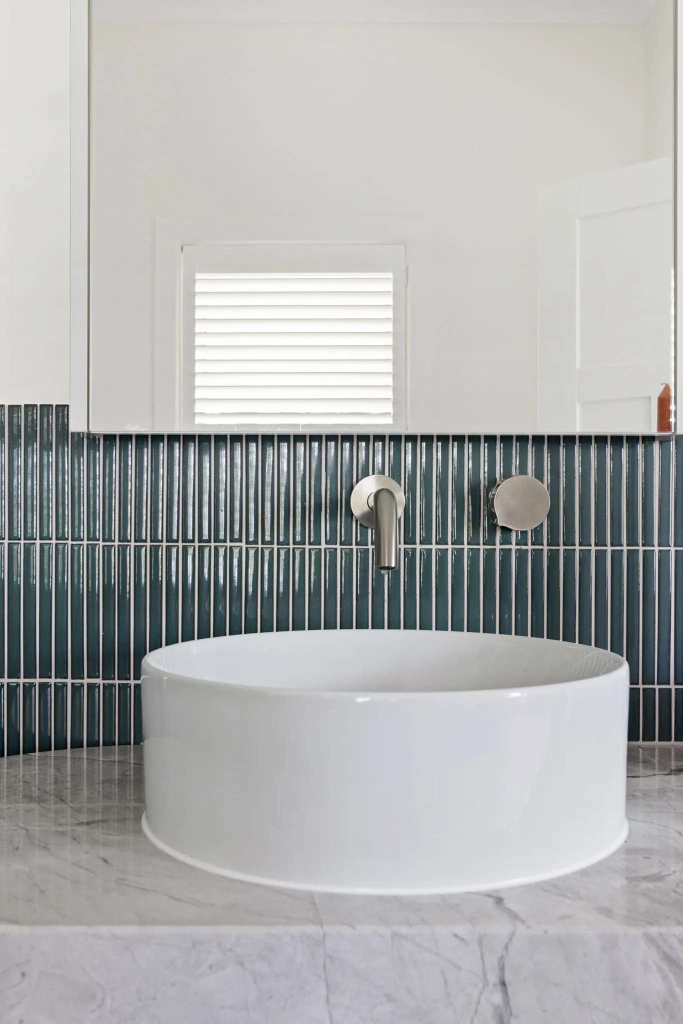 Round freestanding bath on marble with a green tiled splashback and wall-mounted spout