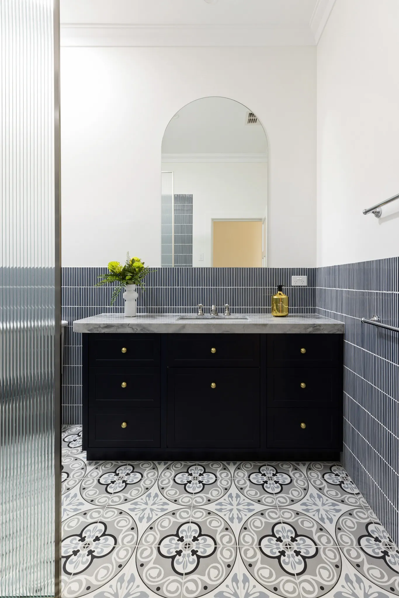 Black shaker vanity with brass knobs, an arched mirror and patterned floor tiles