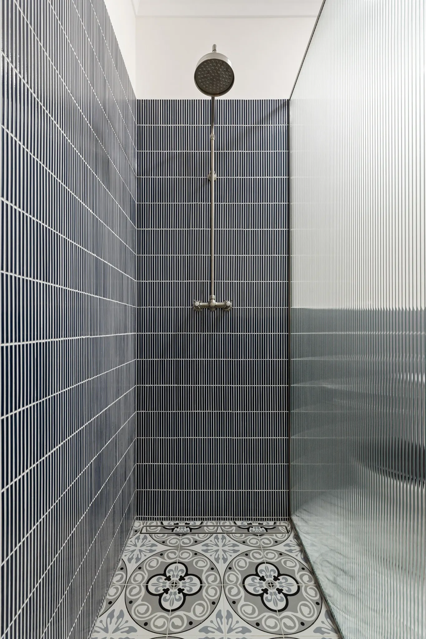 Shower lined in blue tiles with patterned floor tiles and a fluted glass screen
