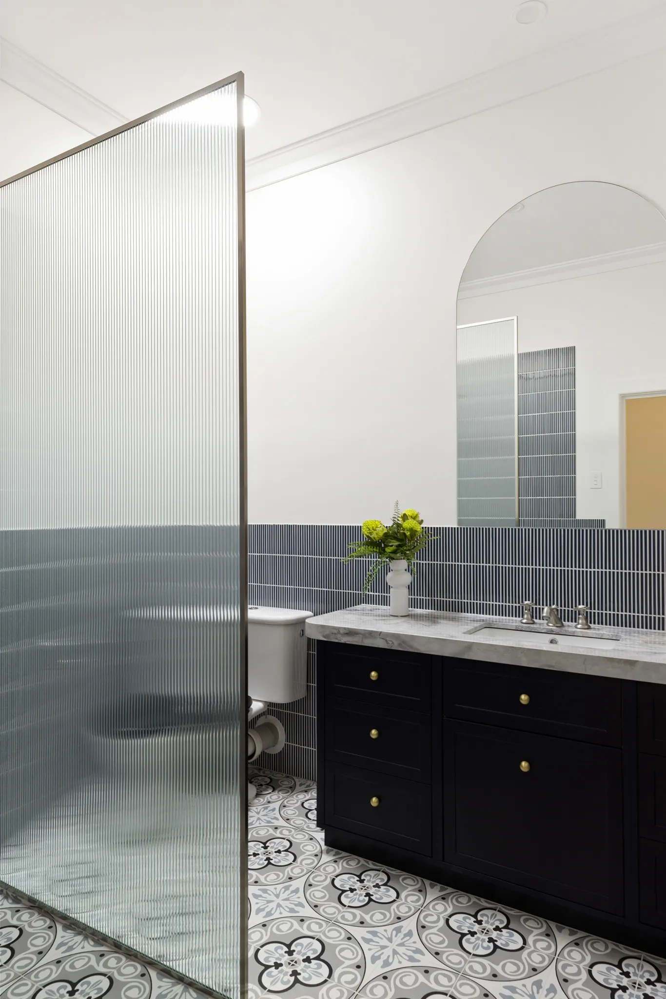 Fluted glass screen dividing the toilet from the black vanity and blue tiled wall