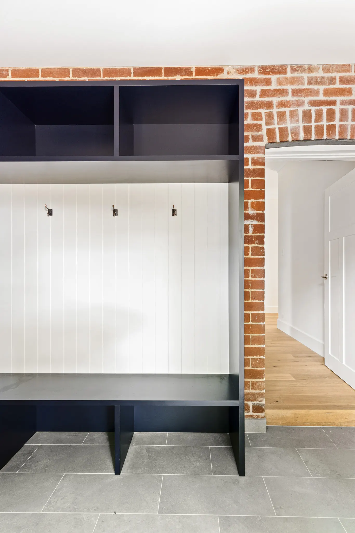 Mudroom joinery in navy with hooks on a v-groove back panel beside exposed brickwork