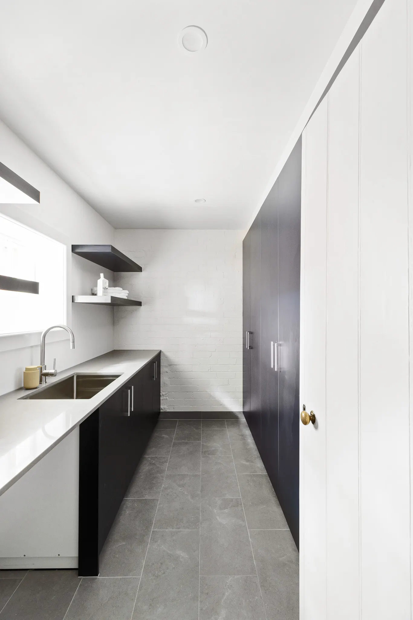 Laundry with dark base joinery, stone benchtop, undermount sink and floating shelves