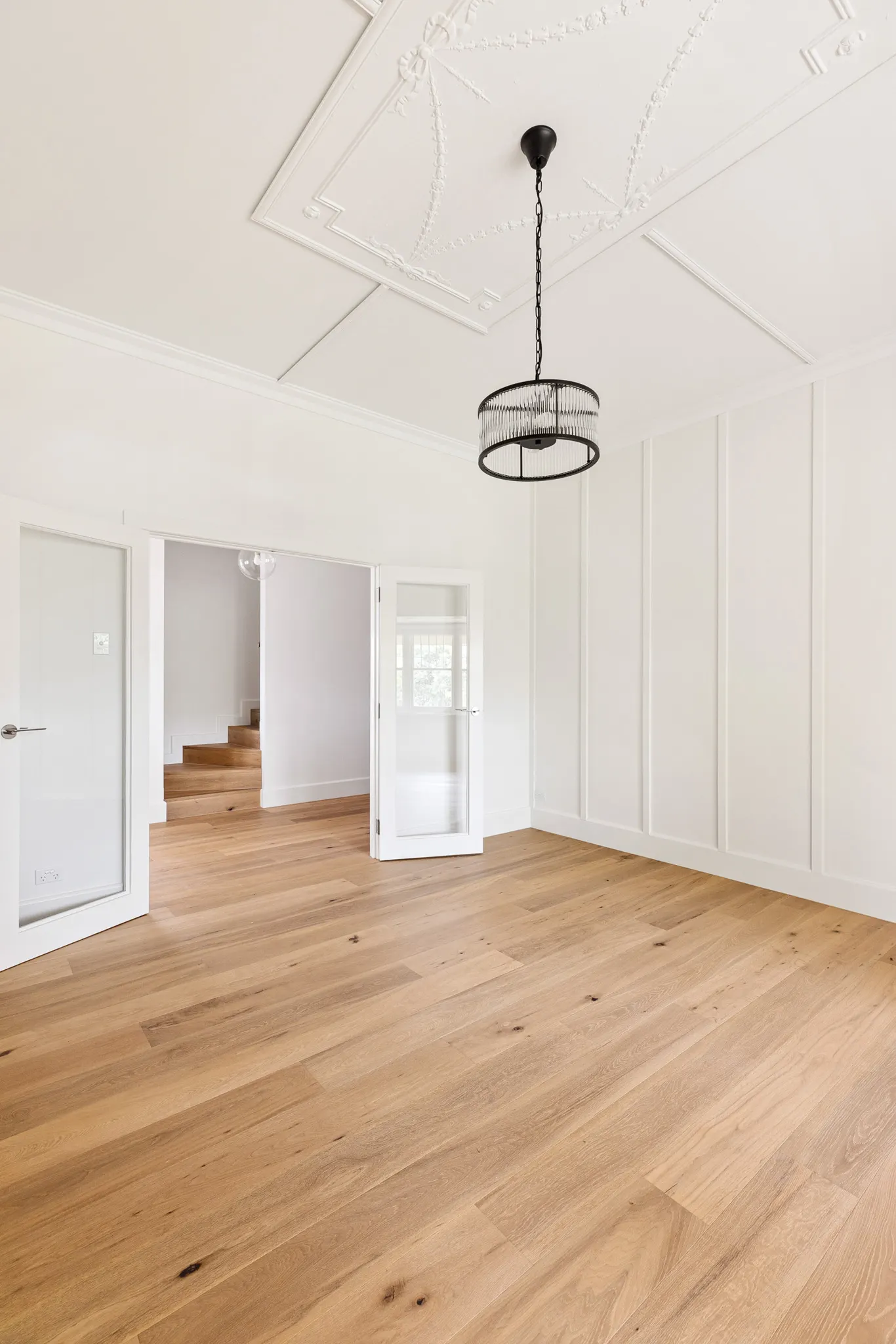Panelled wall and ornate ceiling with glazed doors opening through to the hall