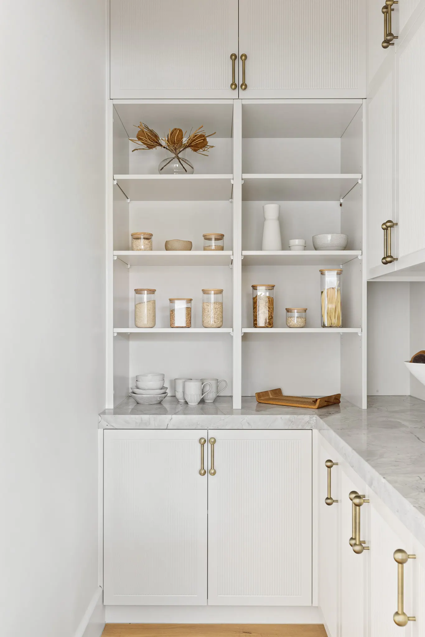 Butler&rsquo;s pantry shelving above a marble bench with fluted doors and brass handles