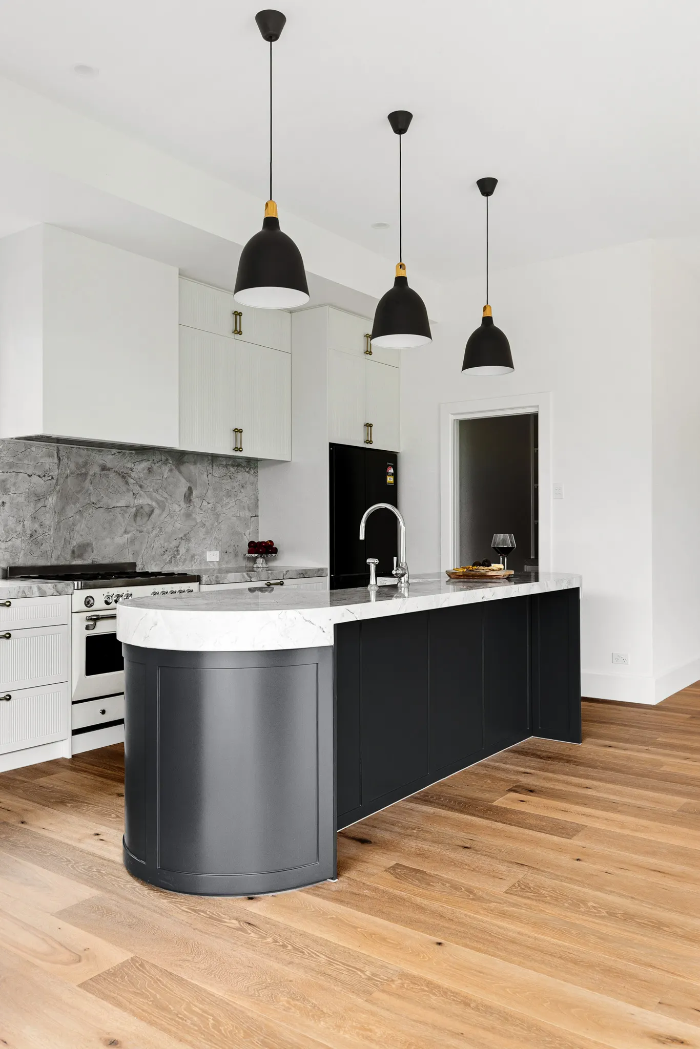 Freestanding cooker and marble splashback with pendants over the curved navy island