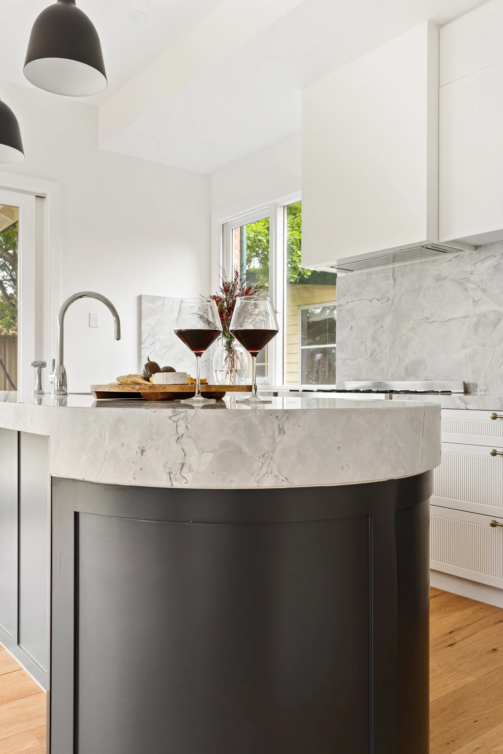 Wine glasses and a grazing board on the marble island benchtop, cooktop beyond