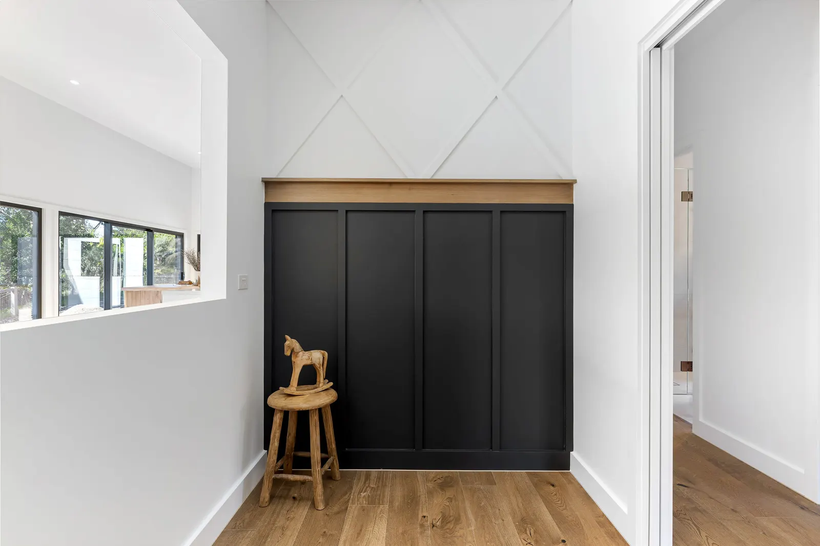 Black panelled built-in joinery with a timber shelf under a raked white ceiling, oak floors