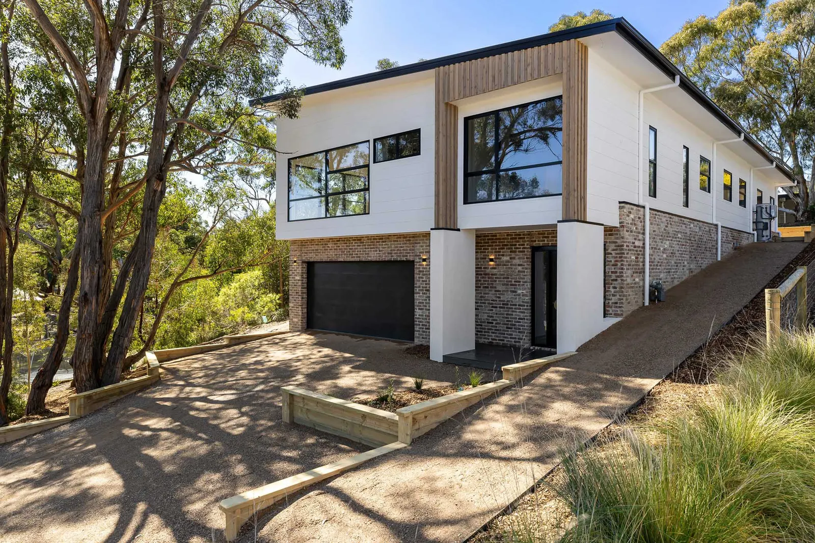 The Dalton St home among gum trees, brick base, white upper storey and black garage door