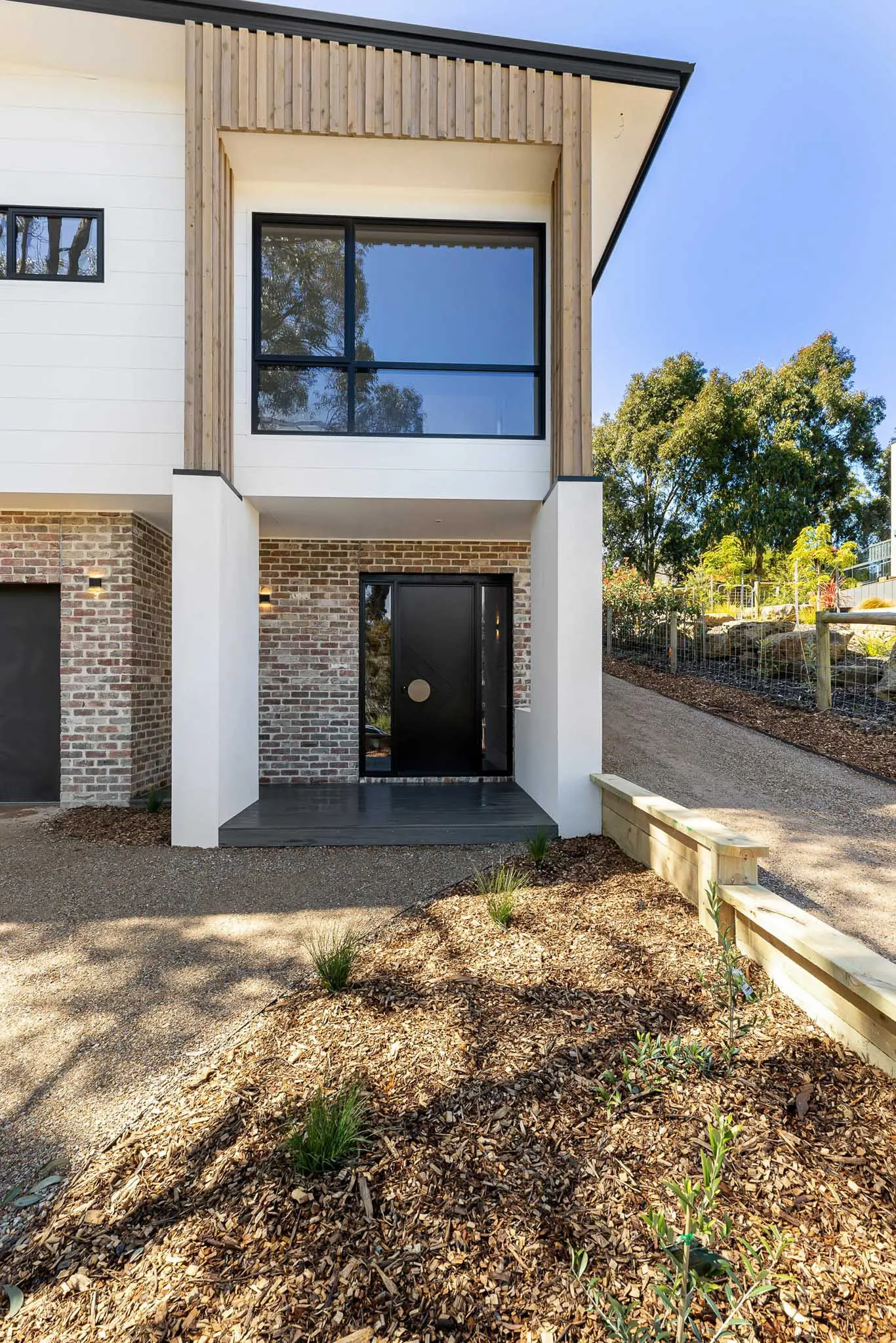 Black entry door with round brass handle set in brickwork, timber battens above