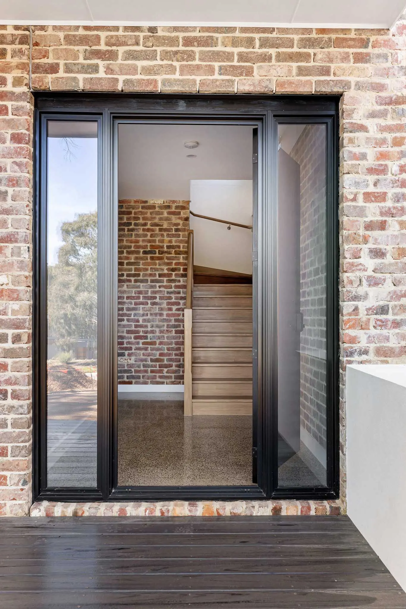 Through the glazed entry door to a timber stair and recycled brick wall beyond