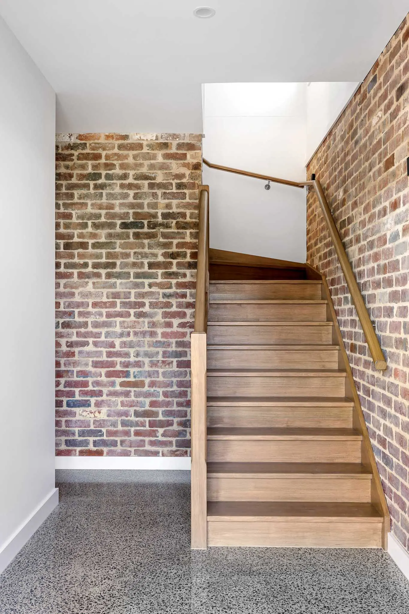 Timber stair with matching handrail rising between recycled brick walls over polished concrete