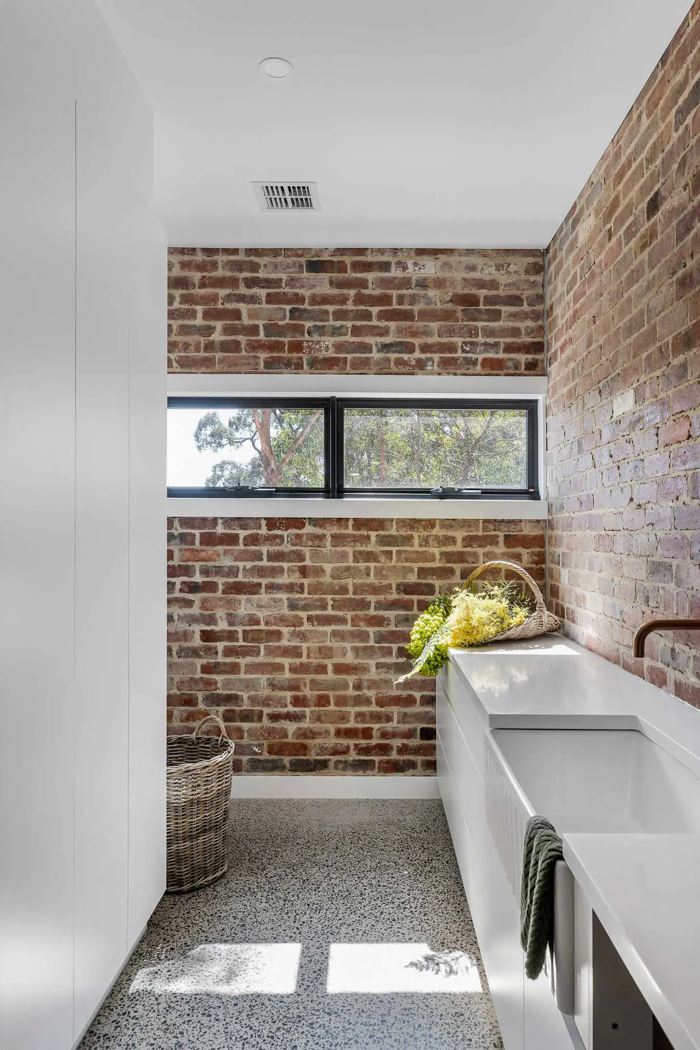 Laundry lined in recycled brick with white joinery, stone benchtop and a long awning window