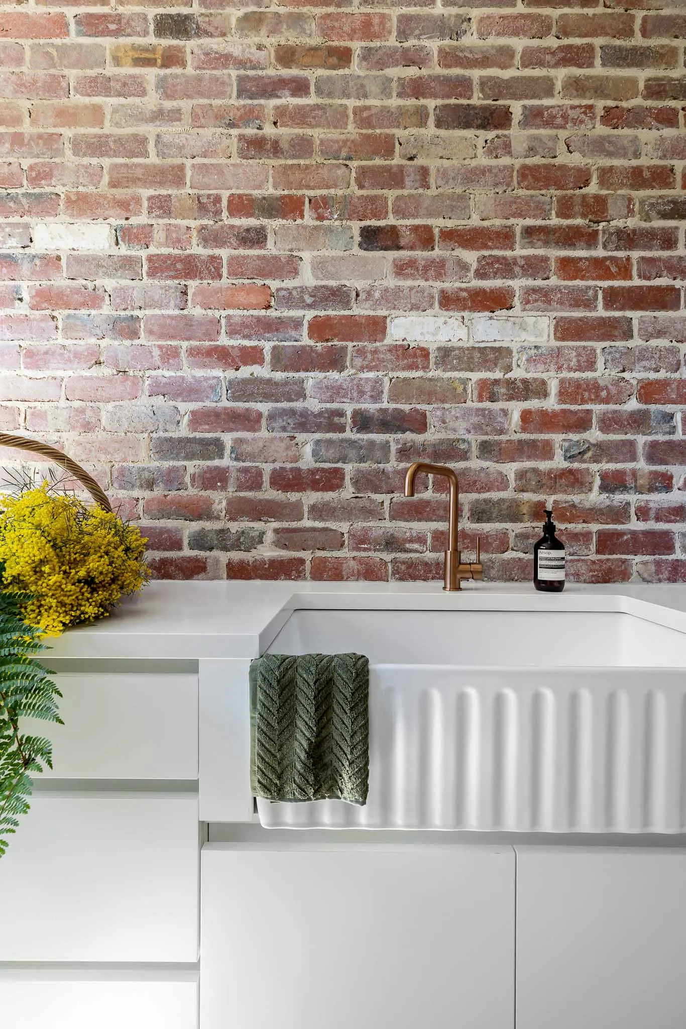 Fluted apron-front sink and brass gooseneck tapware against a recycled brick wall
