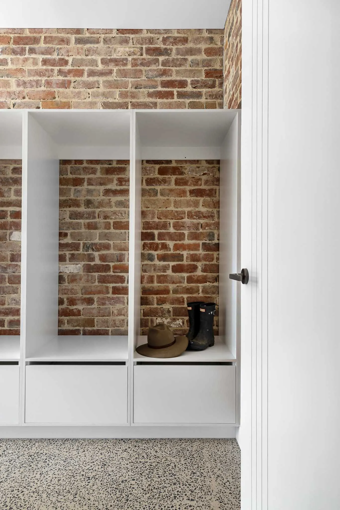 Mudroom lockers in white joinery with bench seat and drawers against recycled brick