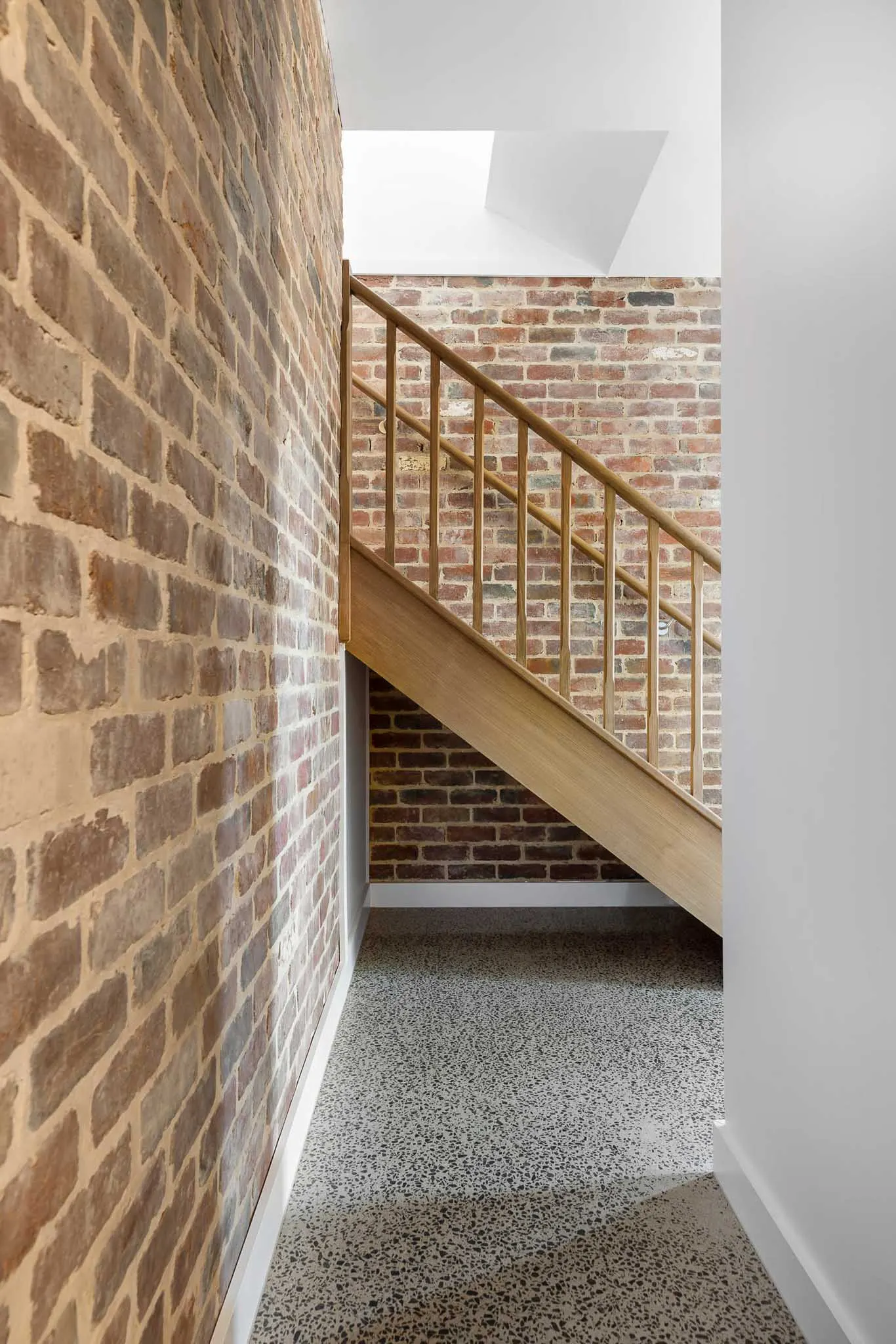 Looking up the timber stair and balustrade, skylight above and recycled brick to both walls