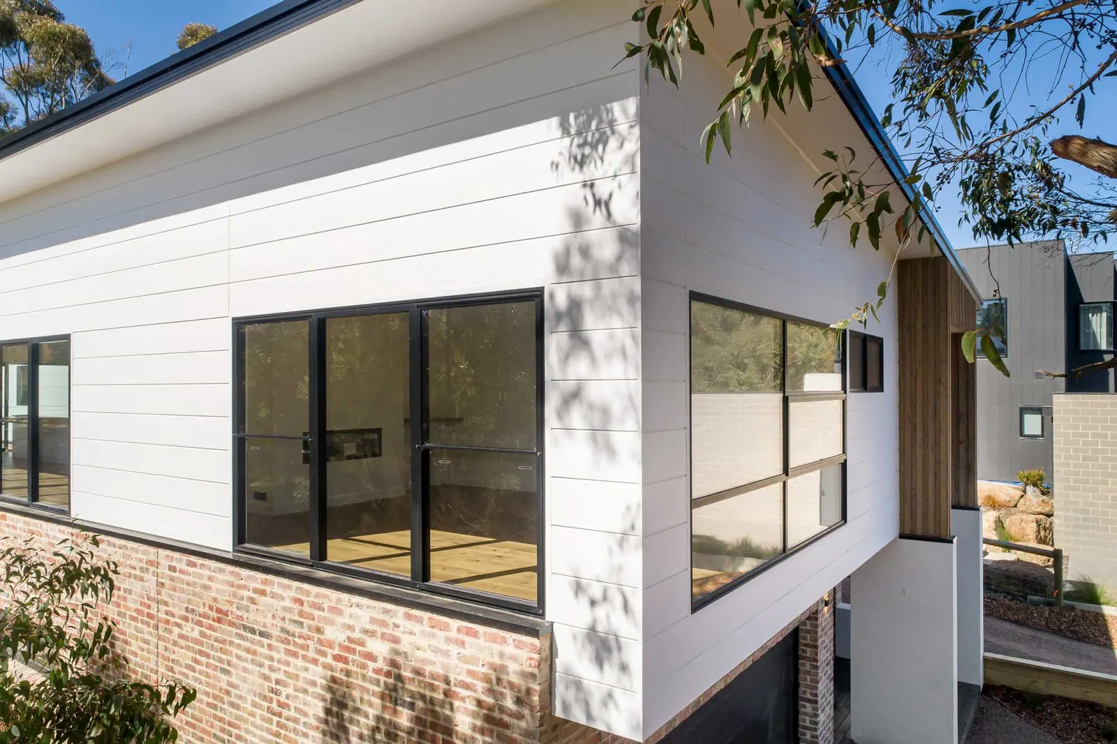 White horizontal cladding meeting brickwork, black-framed windows under a wide eave