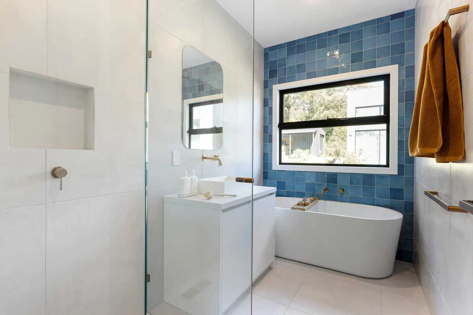 Freestanding bath against a blue tiled wall with black-framed window and brass tapware