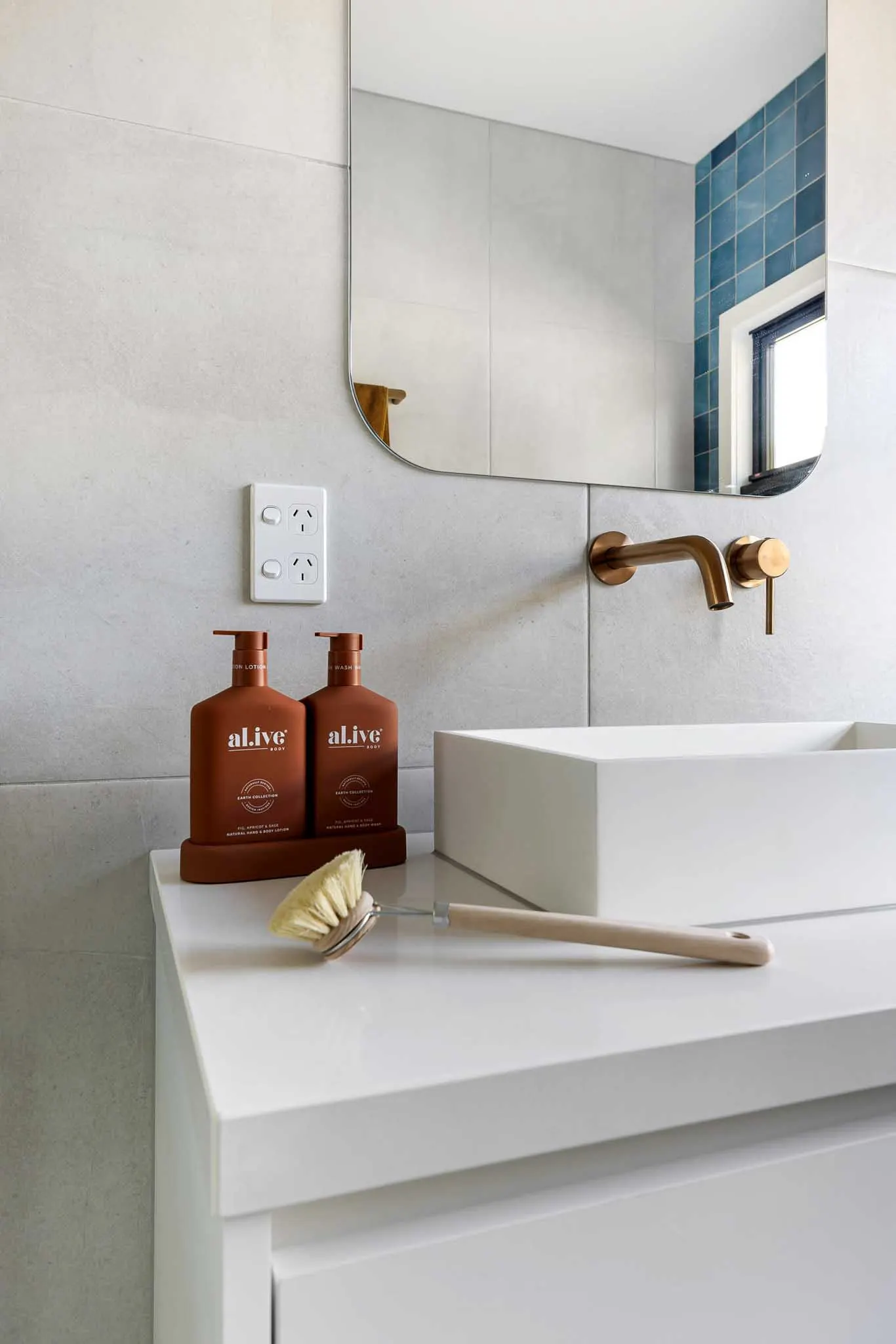 Above-counter basin with brushed brass wall tapware, rounded mirror and stone-look tiles