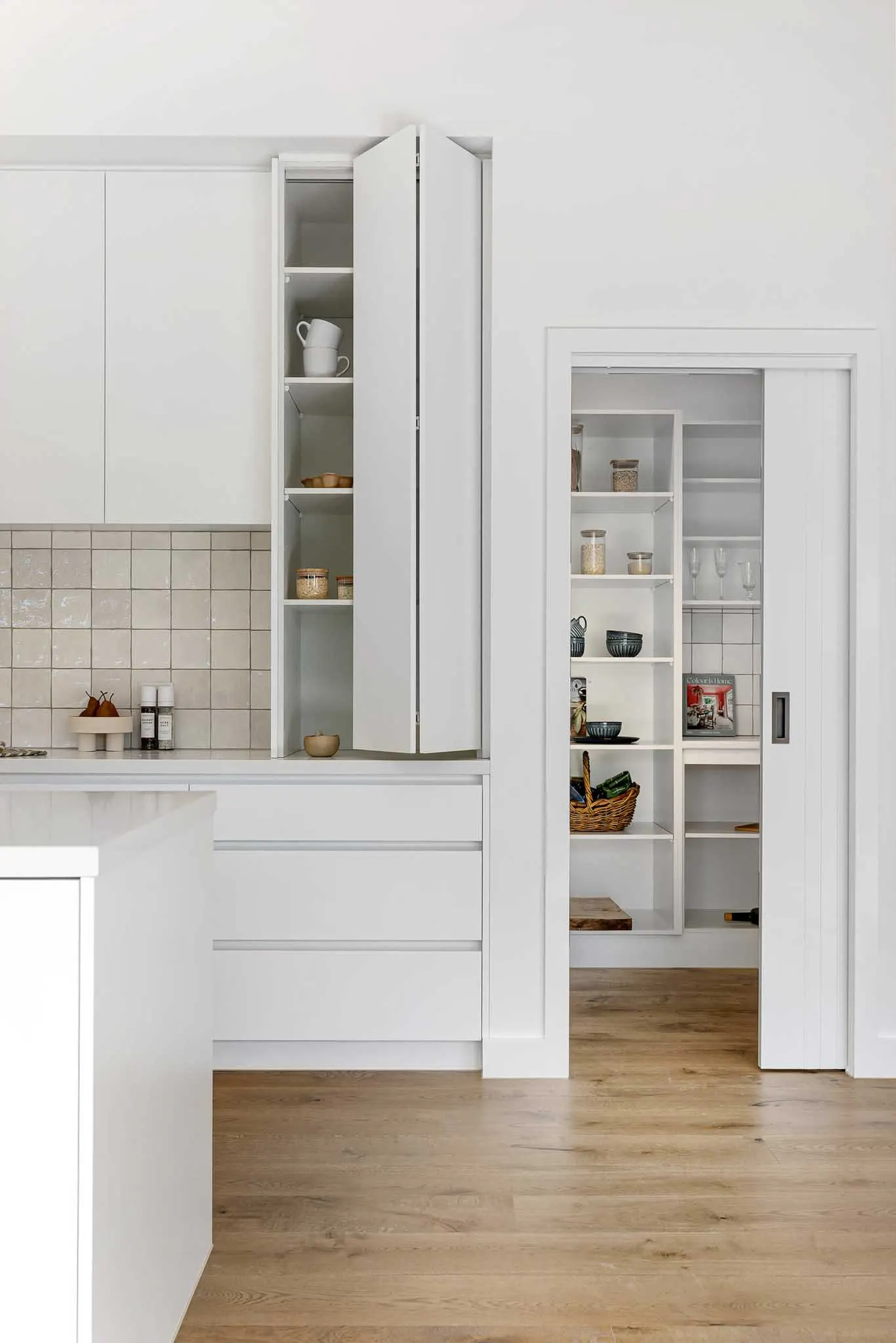White kitchen joinery, glossy square tile splashback and a cavity slider open to the pantry