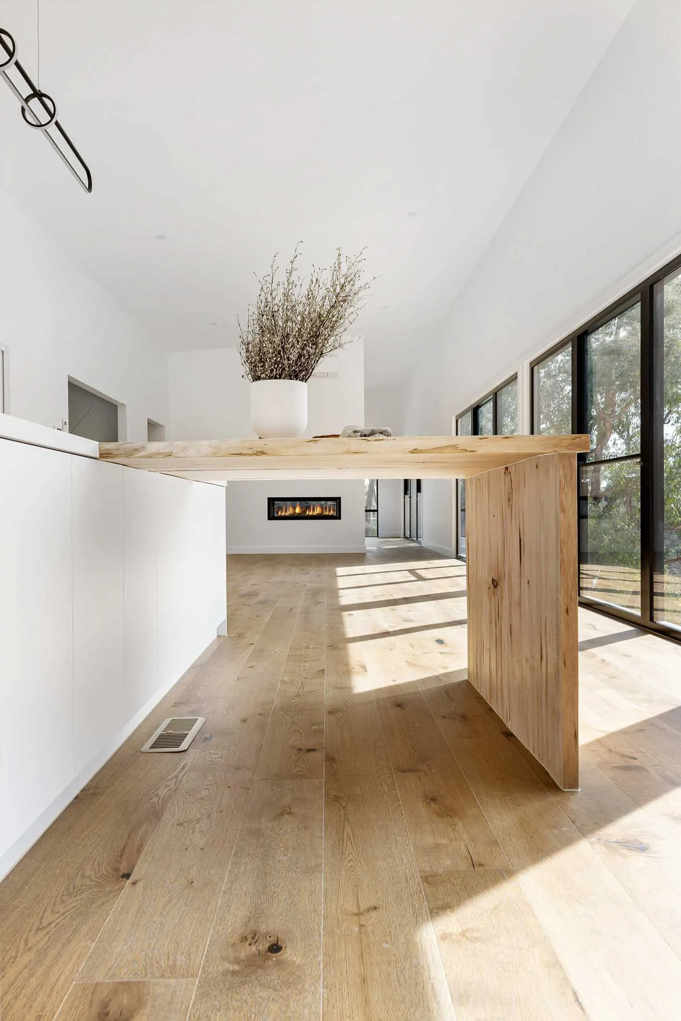 Solid timber table extending from the island, linear pendant above and fireplace beyond