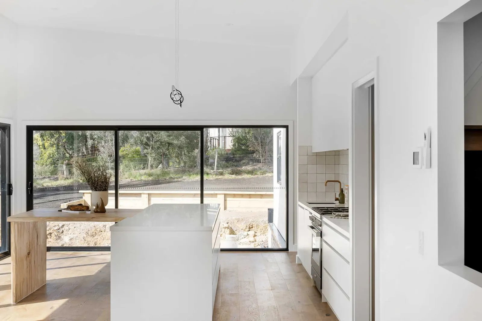 Kitchen island and timber bench looking out through sliding doors to the deck and bush