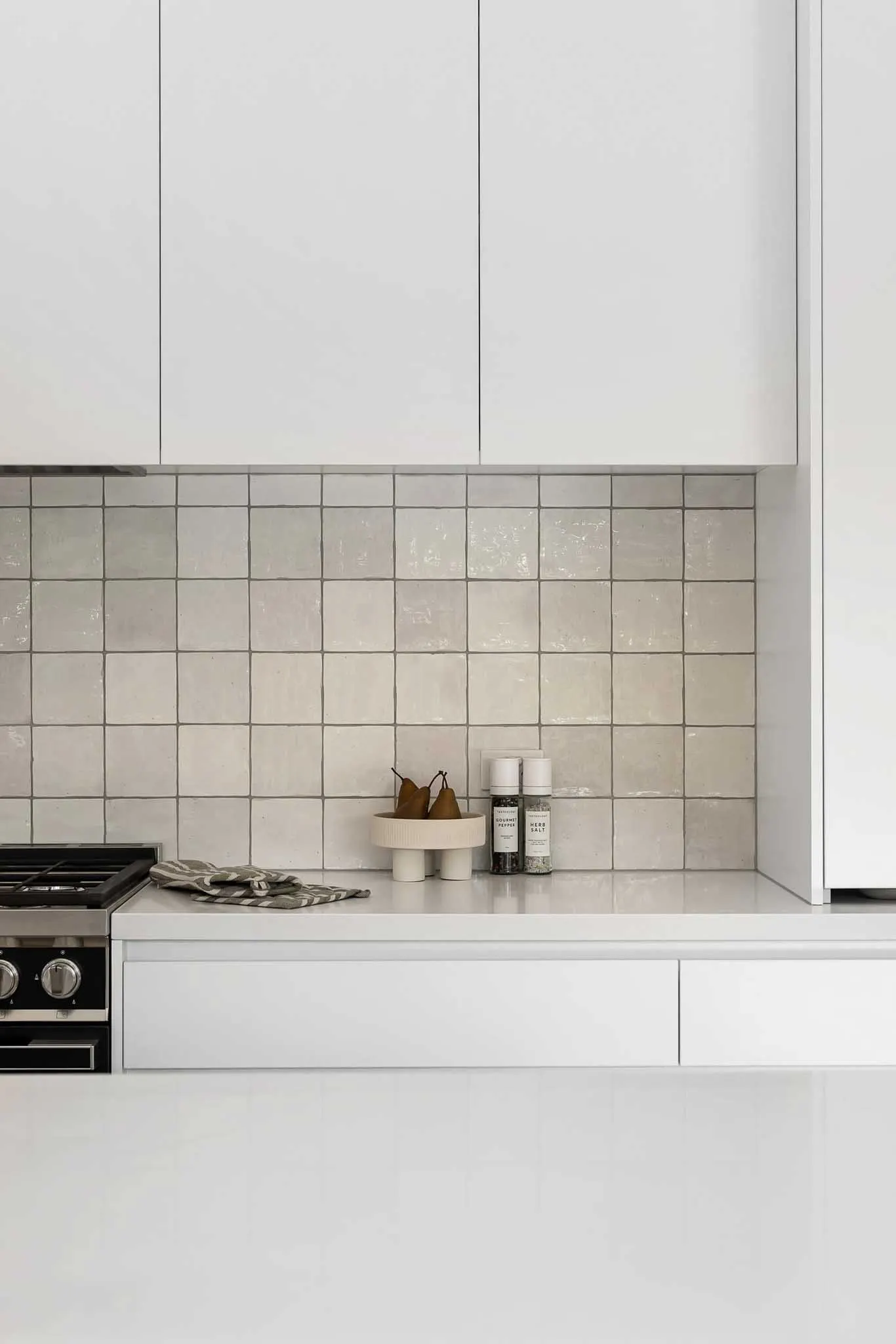 Cream gloss square tile splashback between stone benchtop and white overhead joinery