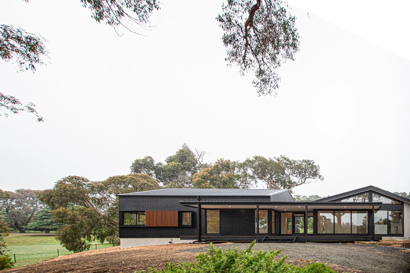 Long low black-clad home with a timber batten panel, seen across a bush paddock