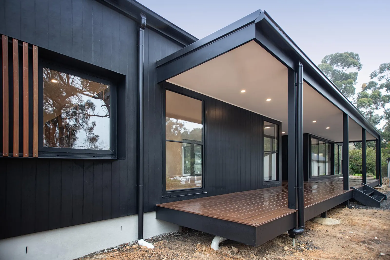 Timber deck and veranda posts against black vertical cladding and a batten window screen