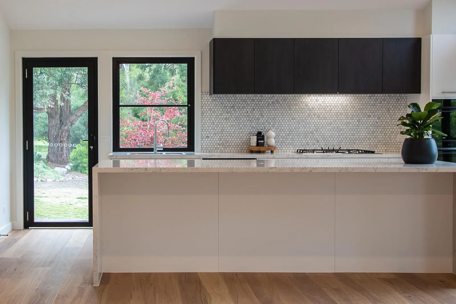 Kitchen with a penny round mosaic splashback, dark overhead joinery and a stone island