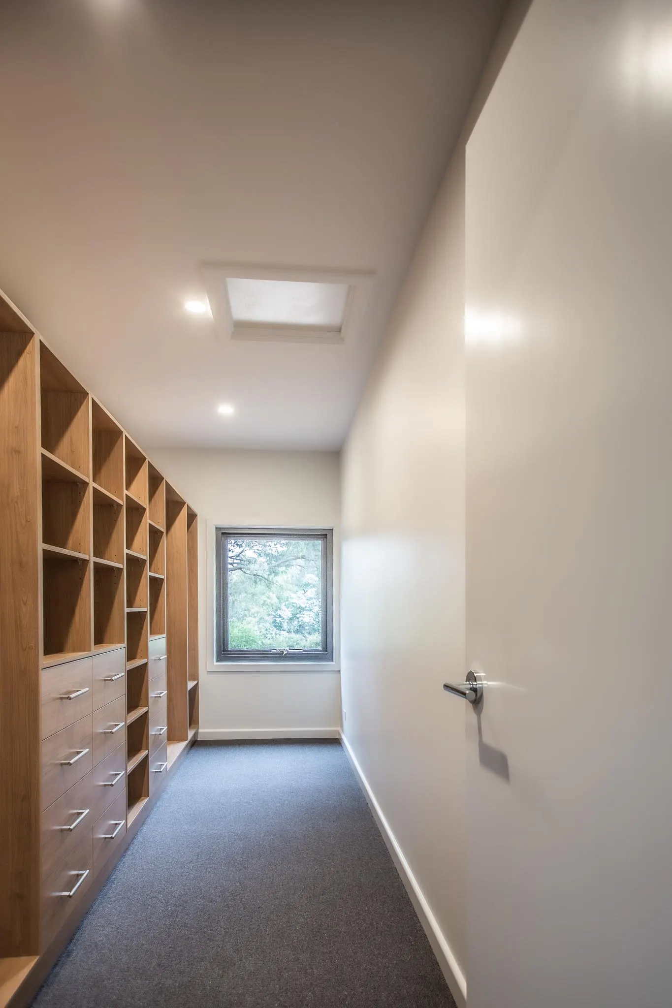 Long walk-in robe lined with timber pigeonholes and drawers, lit by a skylight