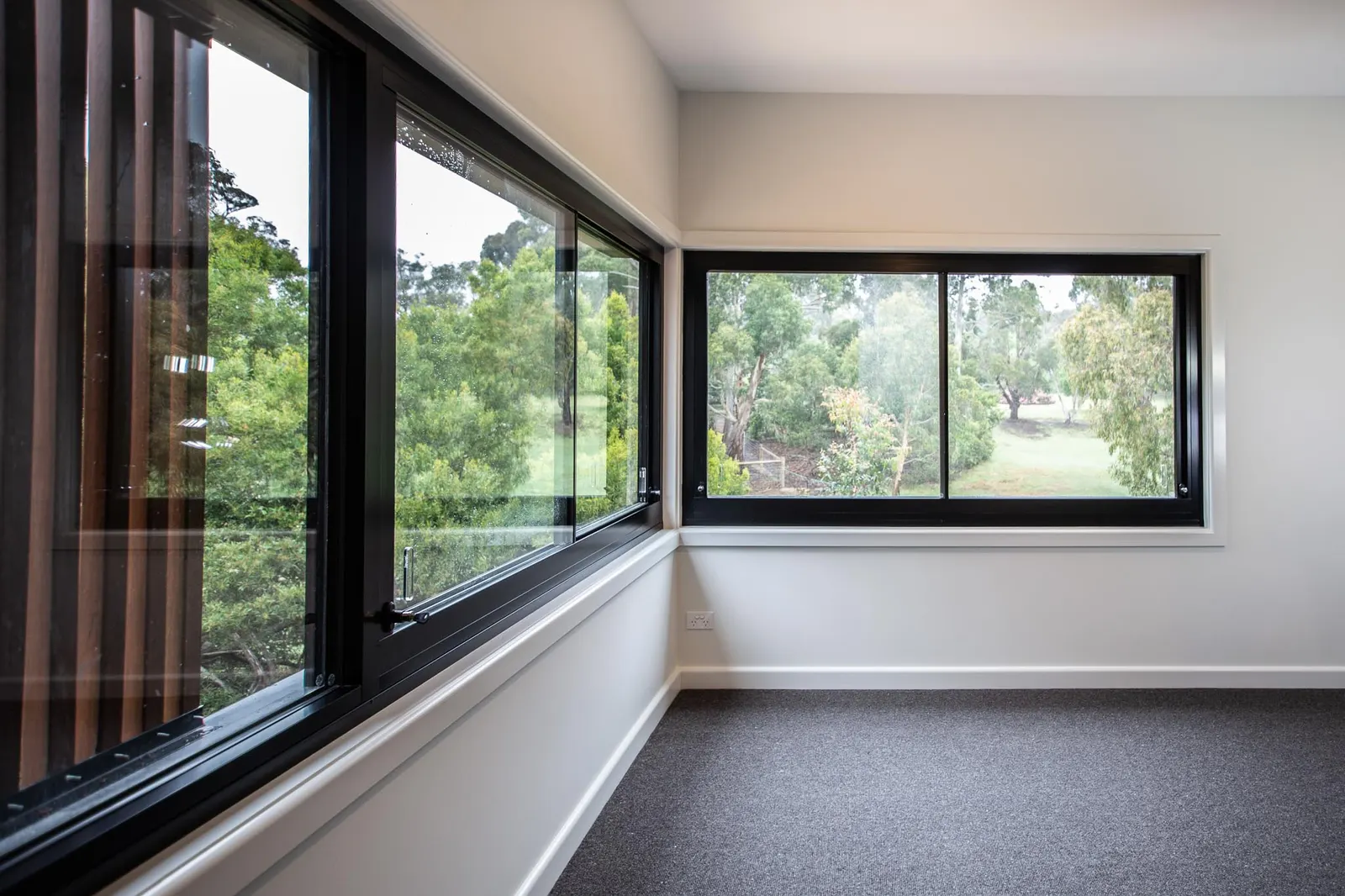 Bedroom corner with two black-framed windows looking over gums and paddock