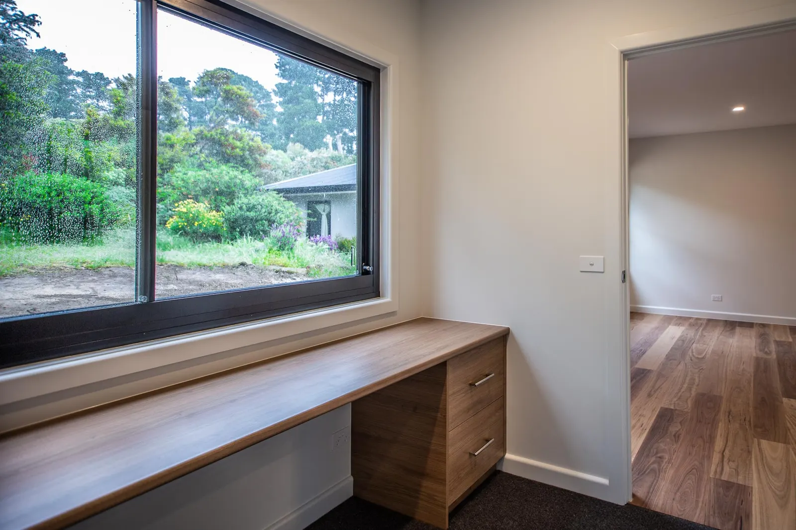 Timber study desk built under a picture window, with drawers and a view to the garden