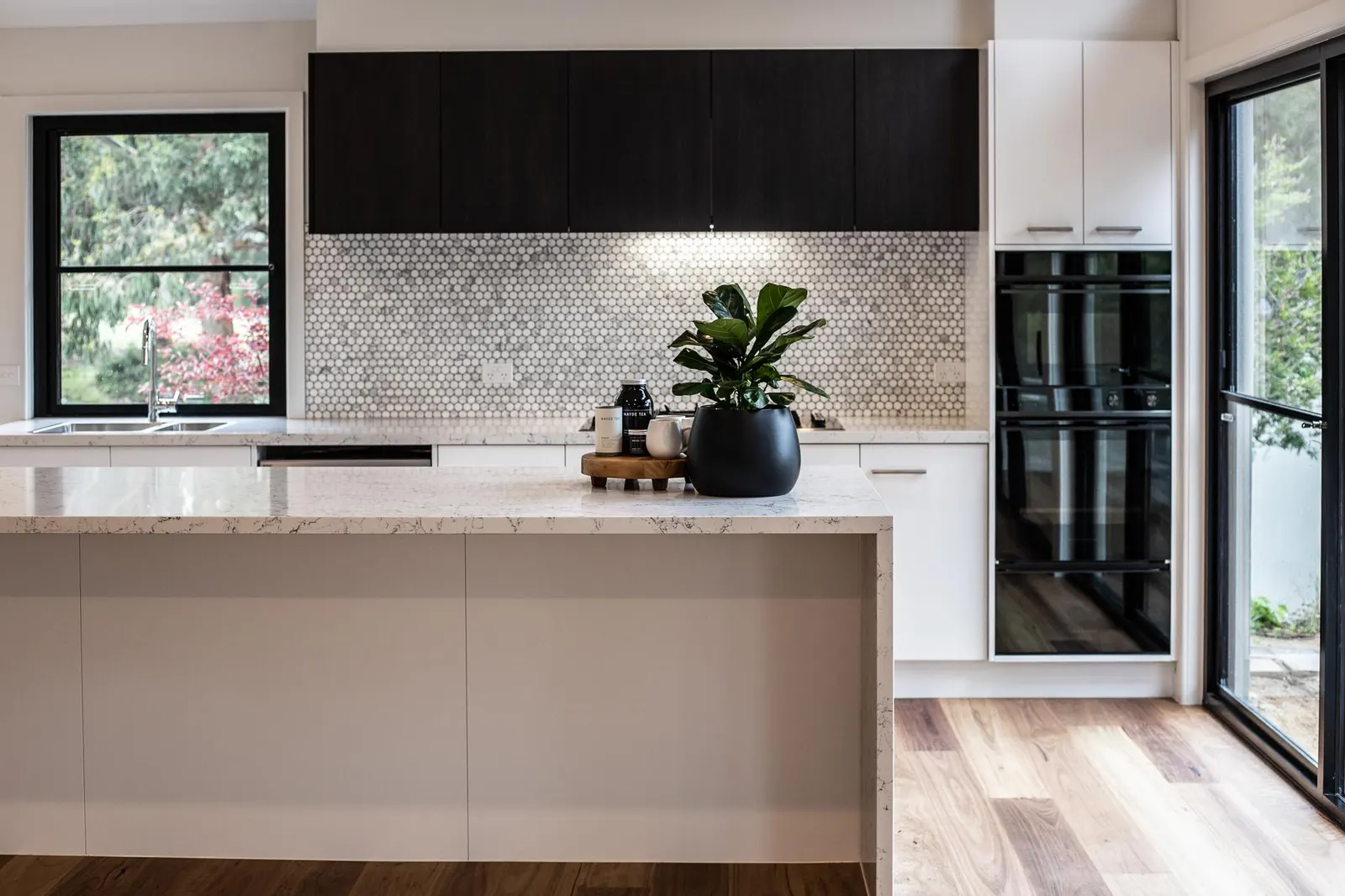Stone waterfall island facing dark overhead joinery and a penny round splashback