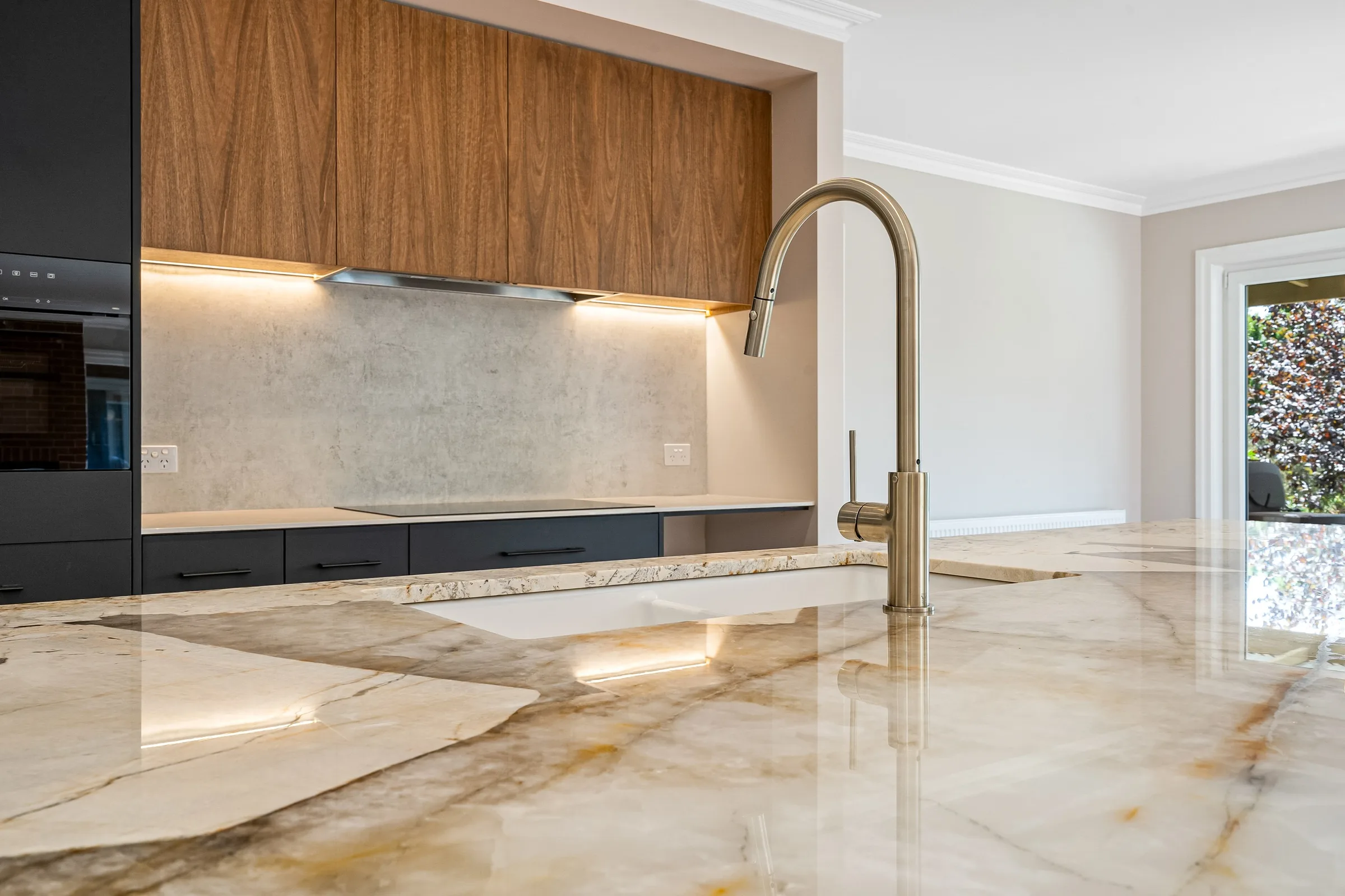 Polished stone island benchtop with a brushed brass gooseneck mixer and undermount sink
