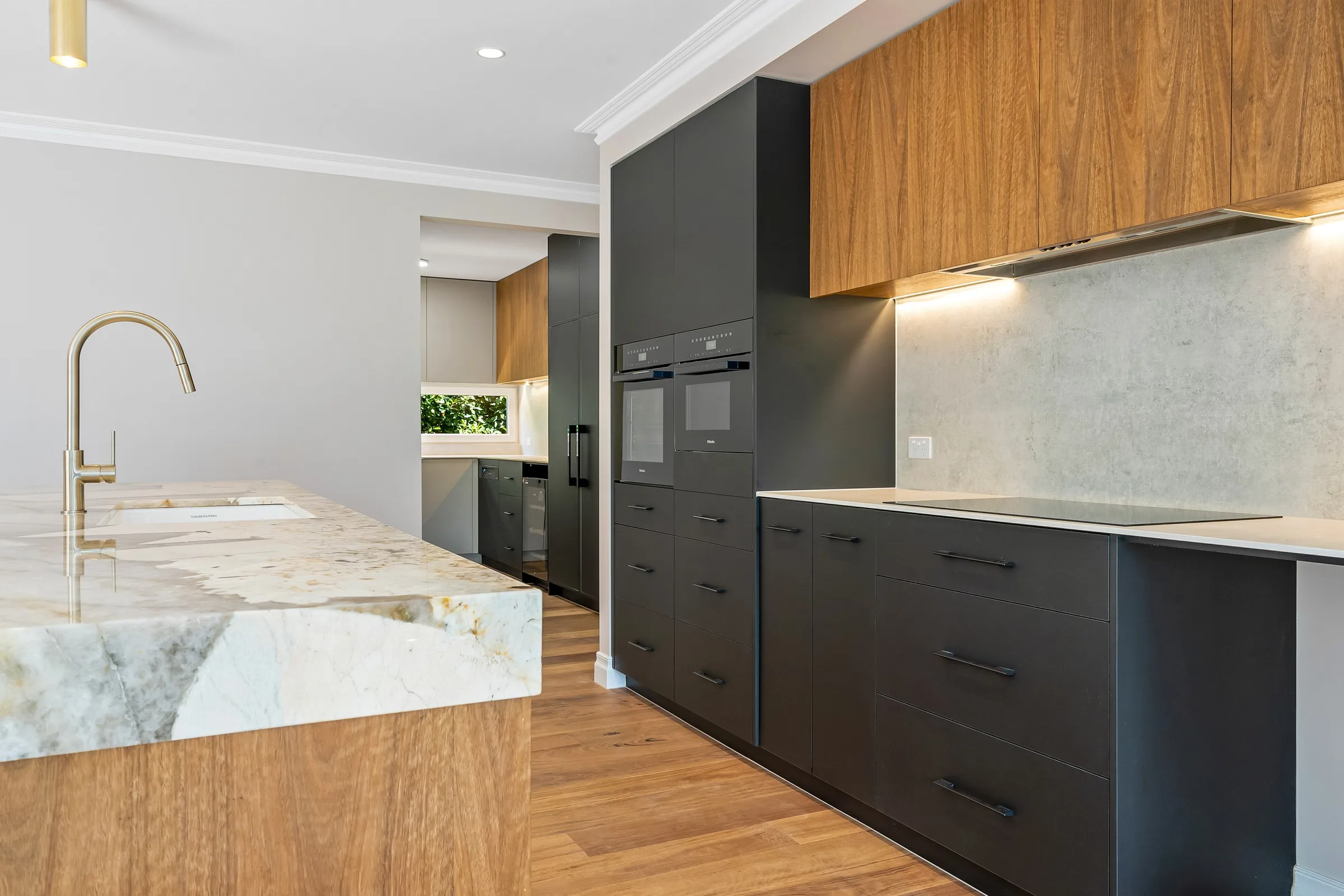 Charcoal drawer banks and stone splashback with timber overheads and a doorway beyond