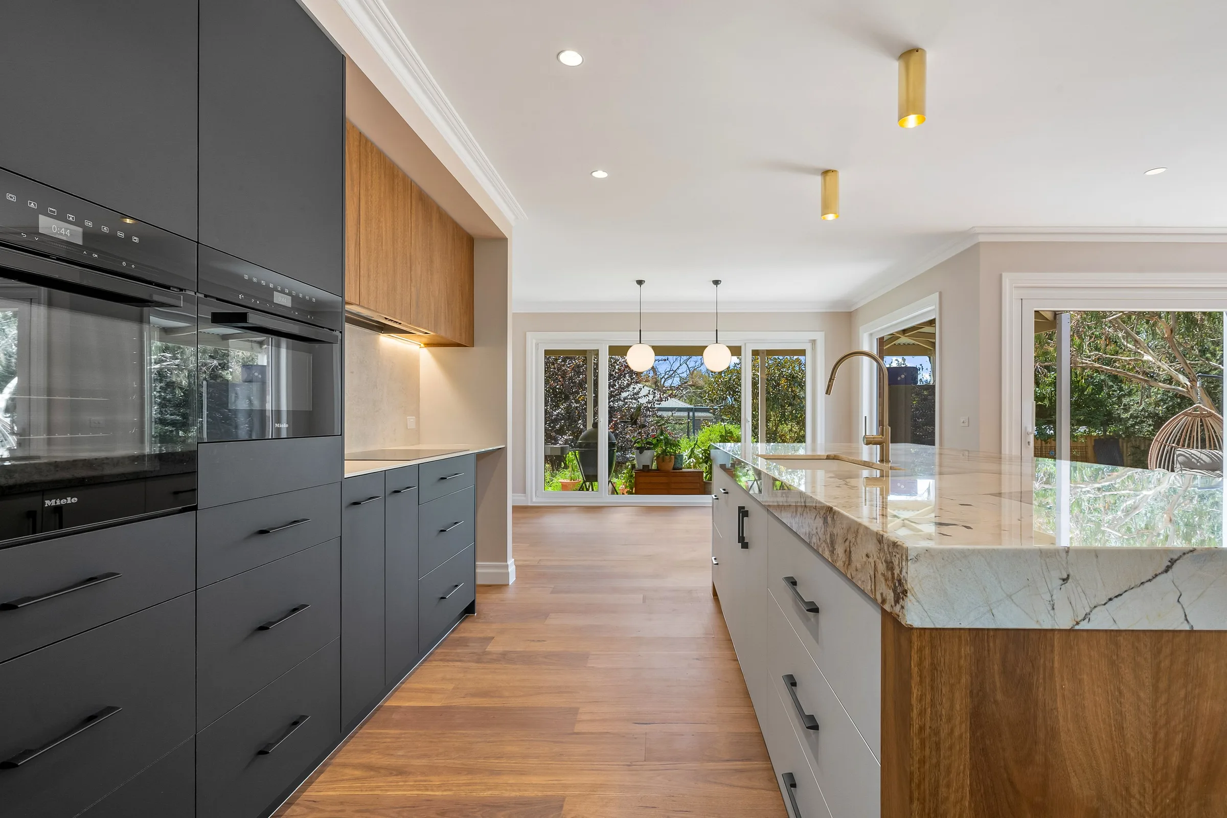 Twin wall ovens in charcoal joinery, brass ceiling lights and windows to the rear garden