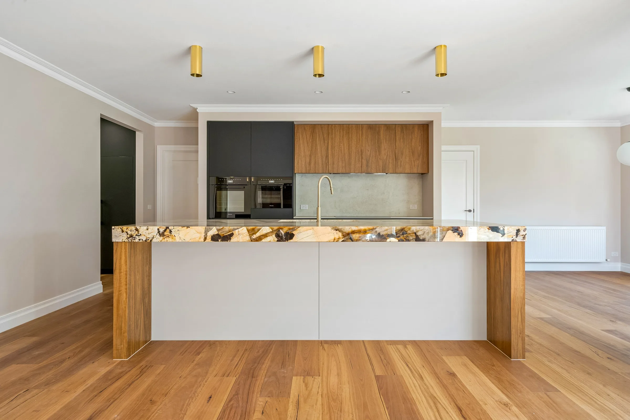 Island in figured stone with timber veneer ends and brass surface-mounted lights above