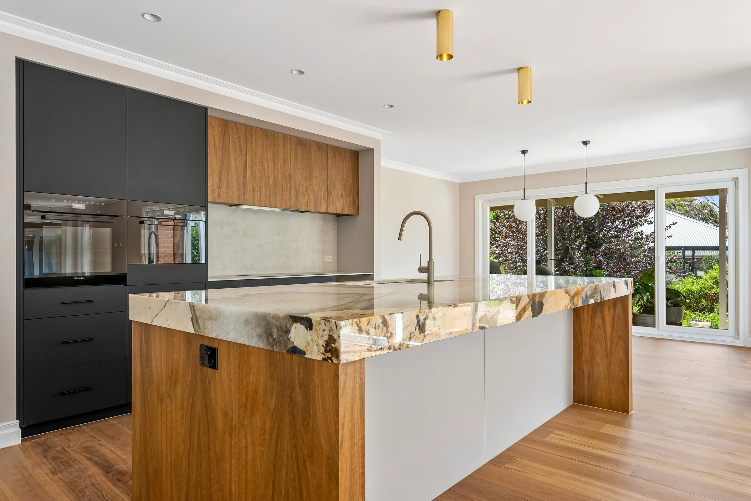 Timber overhead joinery and stone splashback with glass pendants over the island