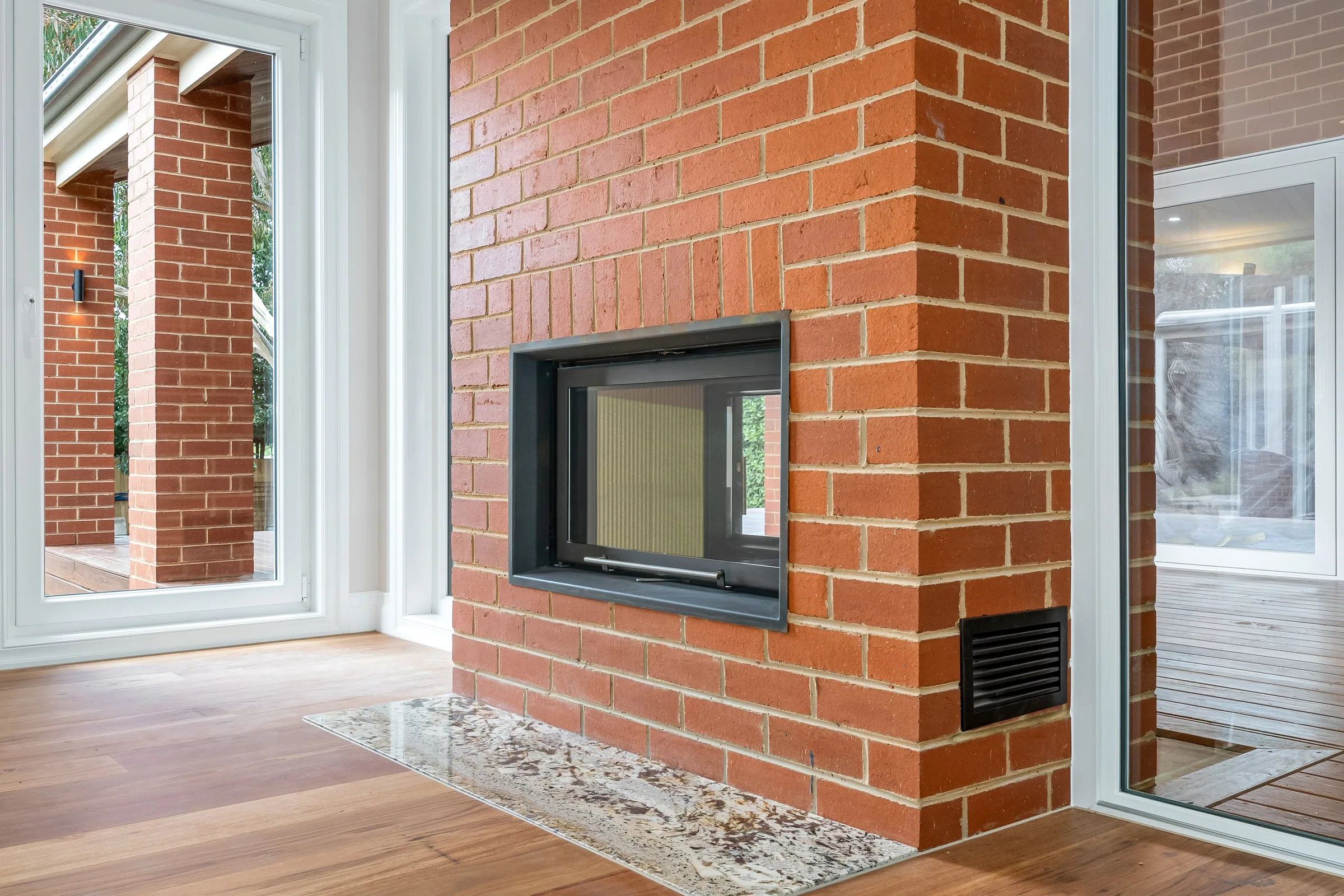 Double-sided brick fireplace with a black firebox and pebble hearth on the timber floor