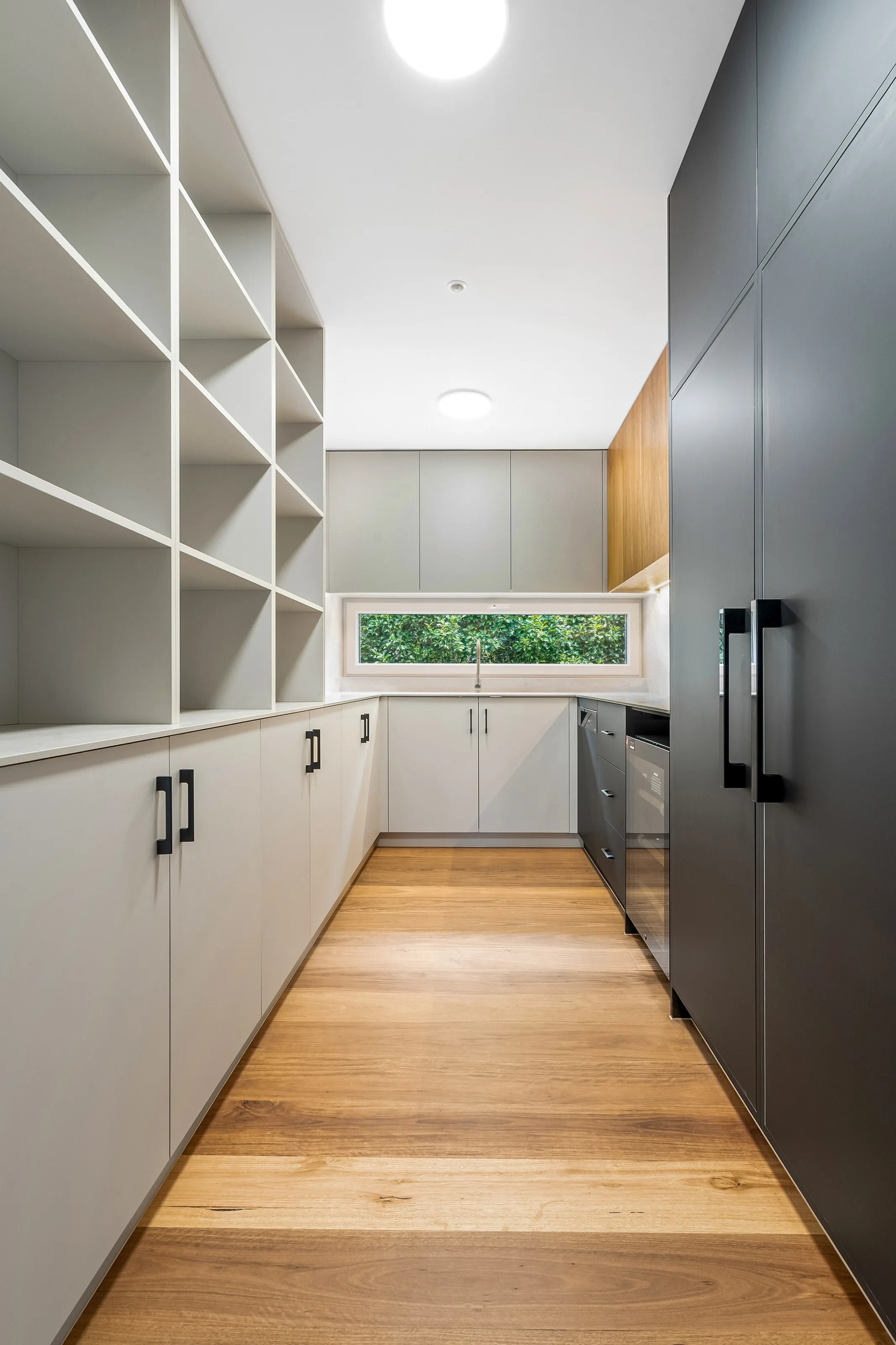 Galley pantry with open shelving cubbies, pale joinery and a highlight window to greenery