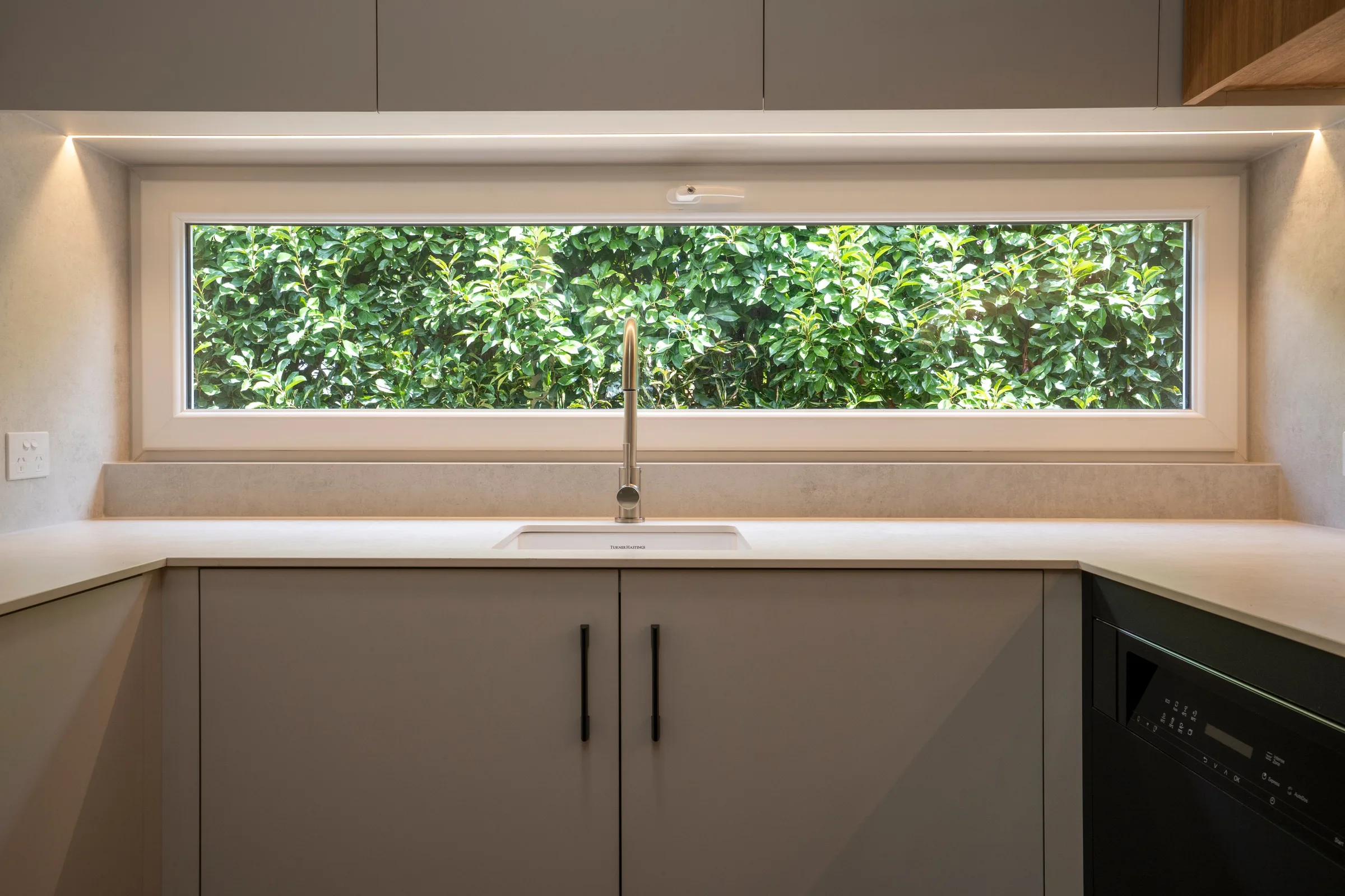 Sink under a long highlight window looking into the hedge, black bar handles below