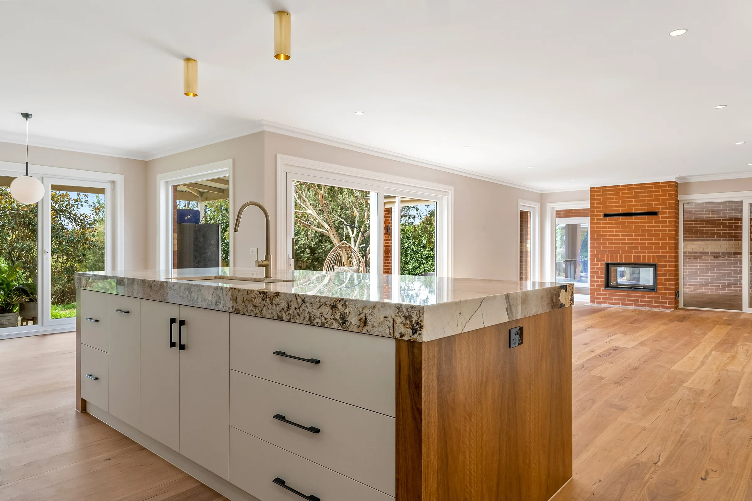 Living and kitchen at Domain Mews, Gisborne, stone island with the brick fireplace beyond