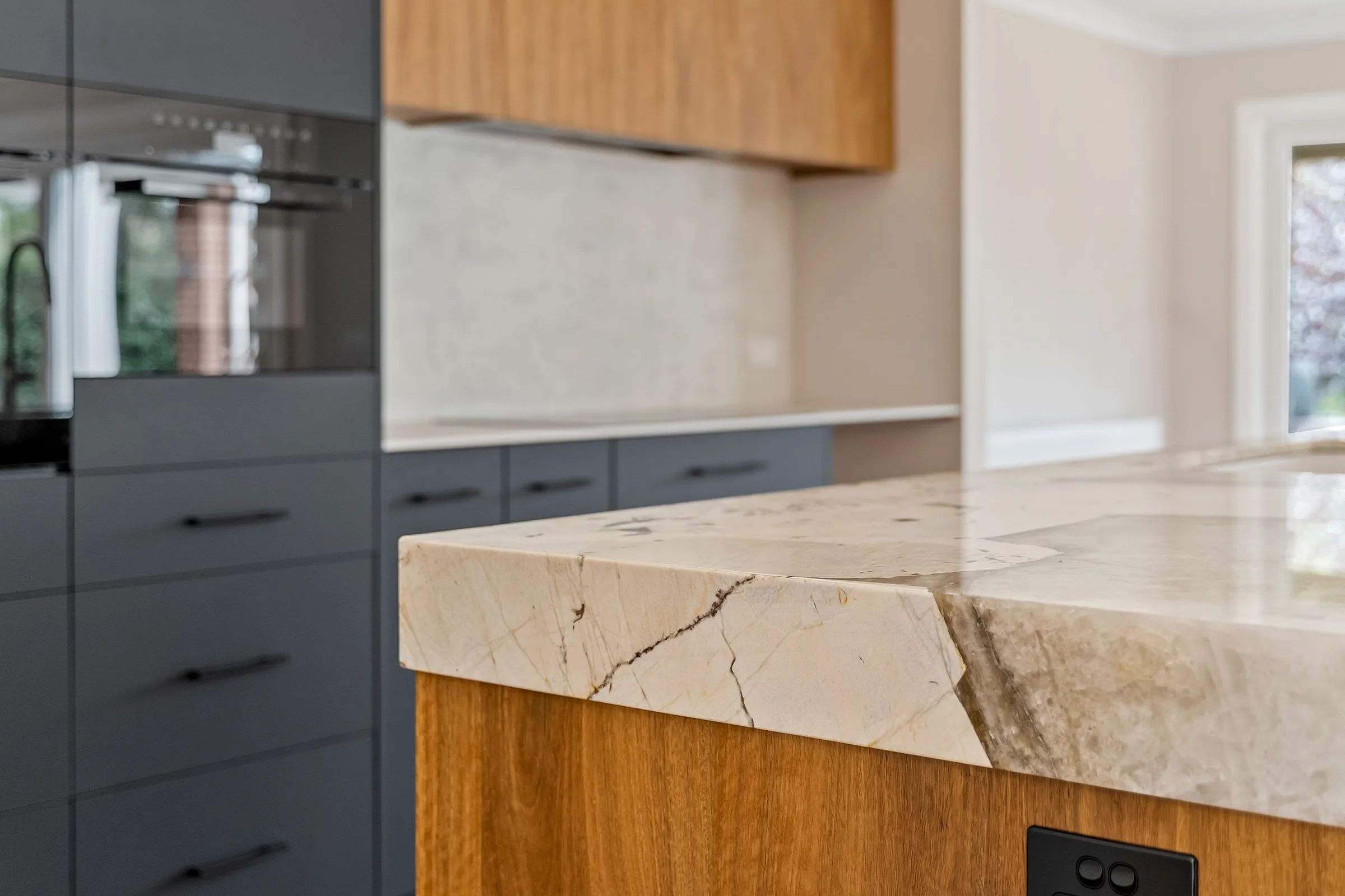 Mitred stone benchtop edge over timber veneer joinery, charcoal drawers behind