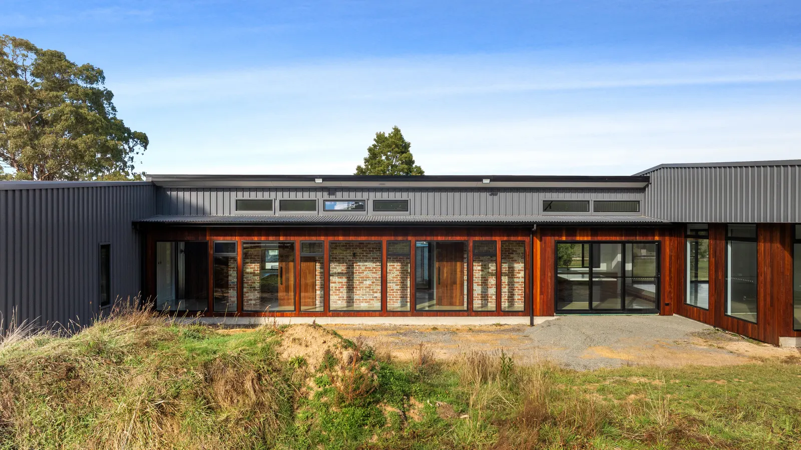 Single-storey home clad in charcoal Colorbond and timber, with recycled brick and full-height glazing along the rear