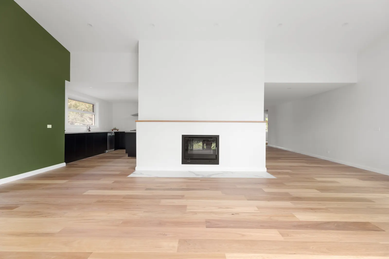 Rendered fireplace with a timber mantel dividing the living area from the kitchen beyond