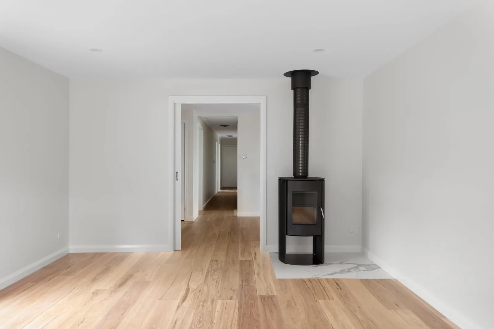 Freestanding black wood heater on a marble hearth beside the opening to the hallway