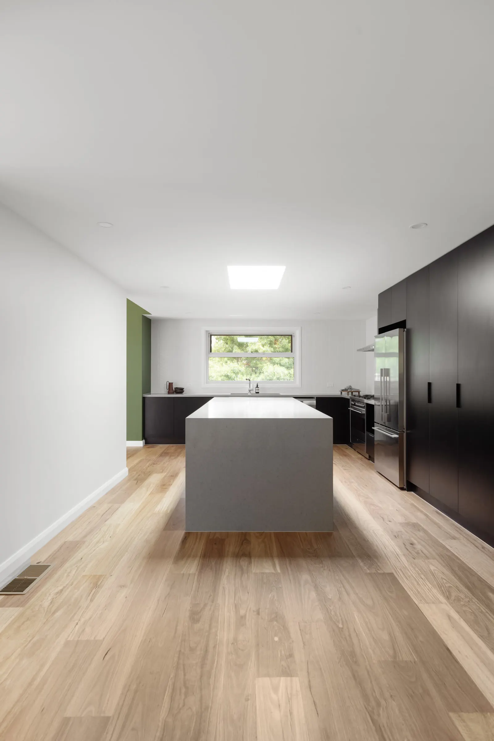 Grey stone island running the length of the kitchen, black joinery and a skylight above
