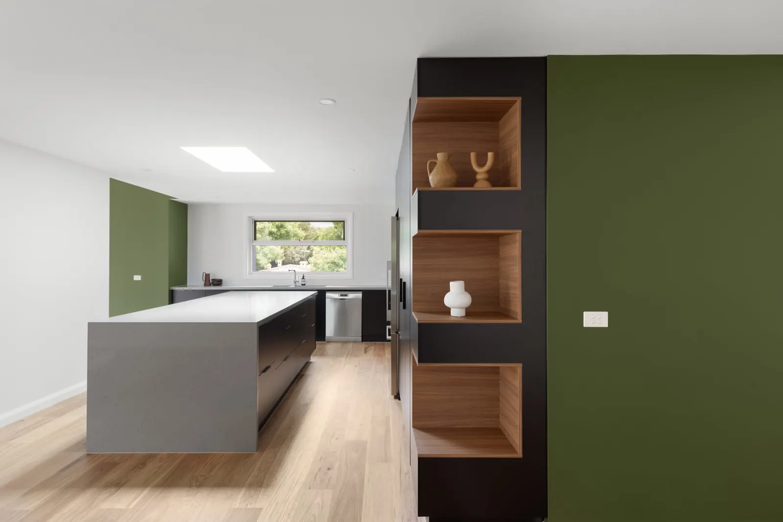 Timber-lined display niches in black joinery beside the green wall, kitchen island beyond